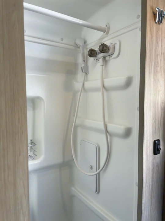 Explore a clean, compact RV rental shower with a handheld sprayer, built-in shelves, and grab bar for comfortable travel.. Ram Winnebago Solis 2023