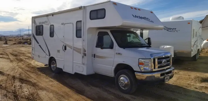 Majestic rv rental (Class C motorhome) on a dirt track, with another camper and mountains in the distance.. Thor Majestic 2013
