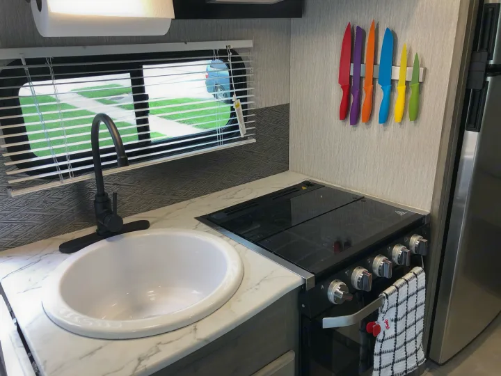 RV rental kitchen: modern sink, stove, marble-look counter, and colorful knives mounted on the wall.. Forest River Coachmen Cross Trail XL 2022