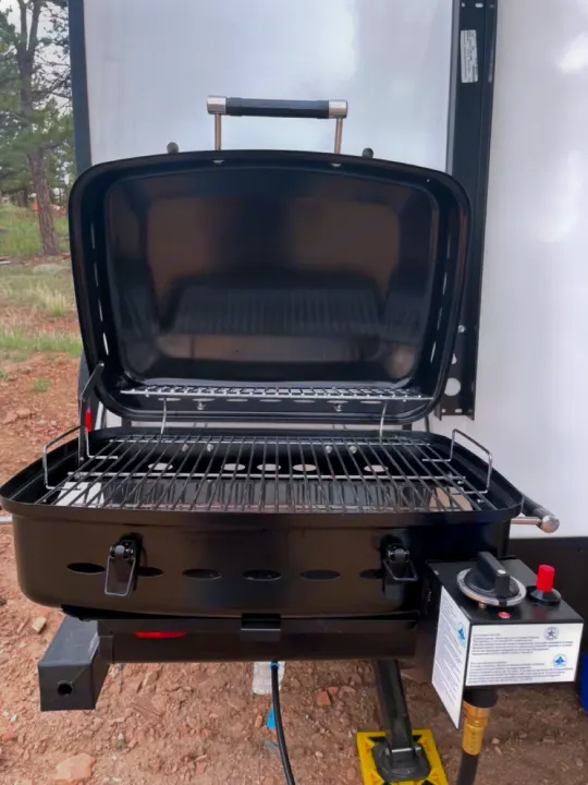 Open black portable gas grill on an RV rental, showing cooking grates and controls. Ideal for campsite outdoor cooking.. Heartland RVs North Trail 2021