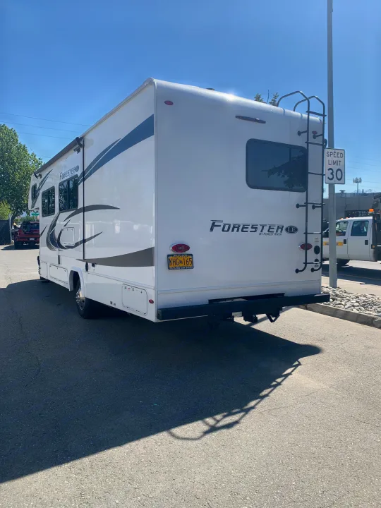 This white Forester RV, seen from the side and rear with an Alaskan plate, parked on asphalt. Ideal for your next rv rental adventure.. Forest River Forester 2551DSLE 2021