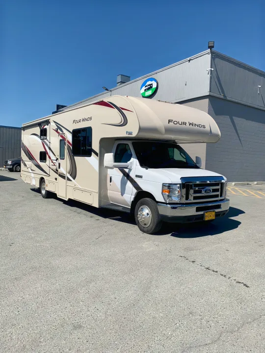 A tan and white Four Winds Class C RV for rent from Alaska RV Rentals, parked outside on a sunny day.. Thor Motor Coach Four Winds 2019