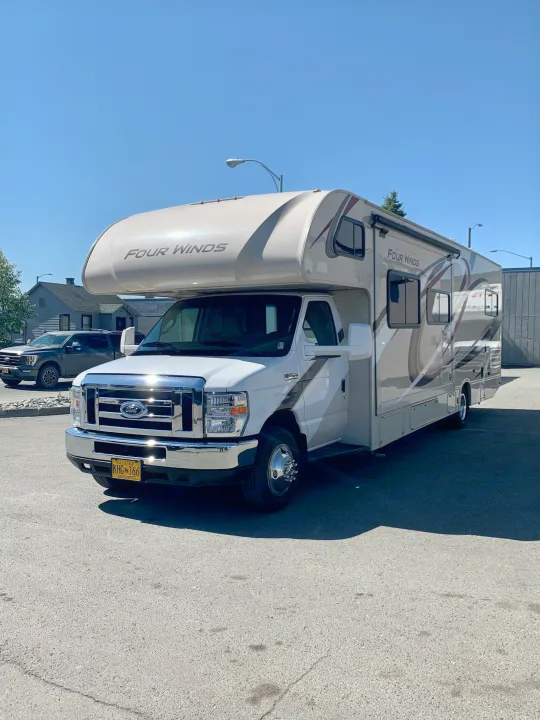 A white Four Winds rv rental motorhome is parked on a sunny day. Its sides feature brown and grey graphics, ready for travel.. Thor Motor Coach Four Winds 2019