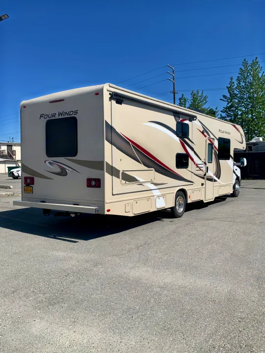 Beige Four Winds RV rental parked on asphalt, featuring stylish decals. Clear sky above, ready for adventure.. Thor Motor Coach Four Winds 2019