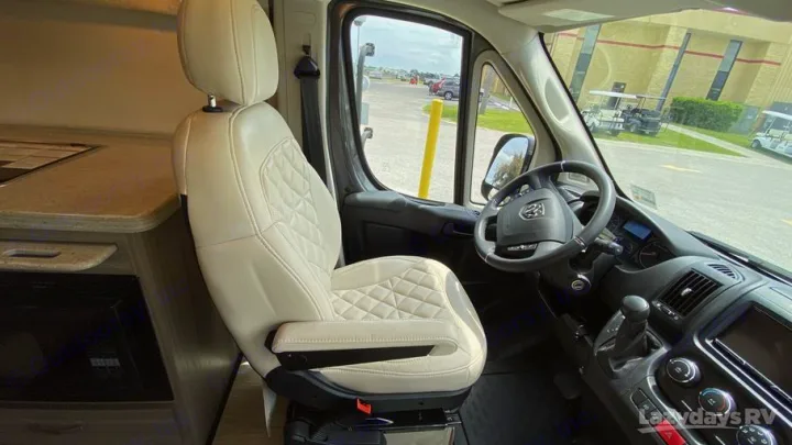 Driver's seat and cockpit of an RV rental, showing a quilted seat, dashboard, and integrated kitchenette counter.. Entegra Coach Ethos 2021