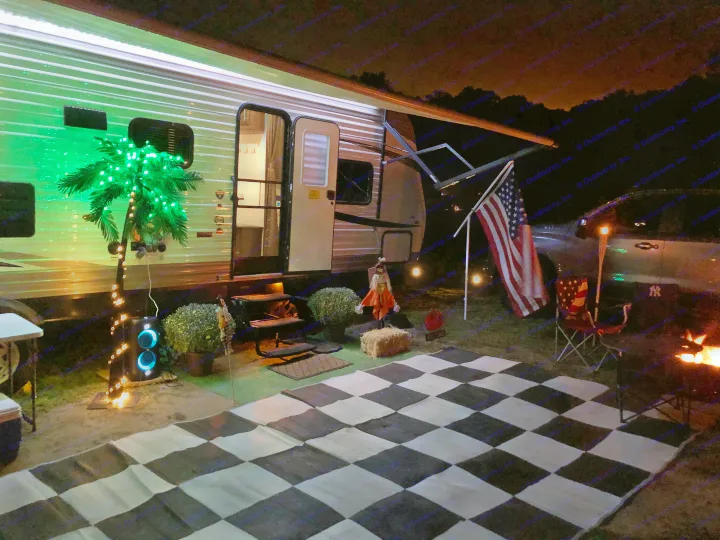 Relaxing RV rental camping setup at night with decorative lights, a checkered mat, US flag, and a warm campfire.. Jayco Flight 2019