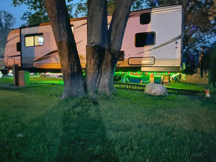 RV rental glamping: A travel trailer glows with red/green lights at night, parked by trees, TV visible inside.. Jayco Flight 2019