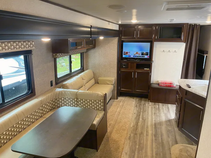 Spacious RV rental interior featuring a comfy living area with a U-shaped dinette, TV, and ample storage cabinets.. Jayco Flight 2019