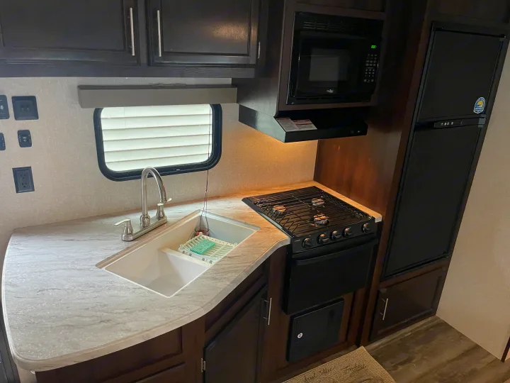 Inside an **RV rental**: a well-equipped **kitchen** featuring a **sink**, **stove**, **microwave**, and **refrigerator**.. Jayco Flight 2019