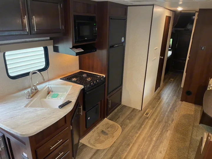 RV rental interior with a bright kitchen, showcasing a sink, stove, microwave, refrigerator, and a hallway extending back.. Jayco Flight 2019