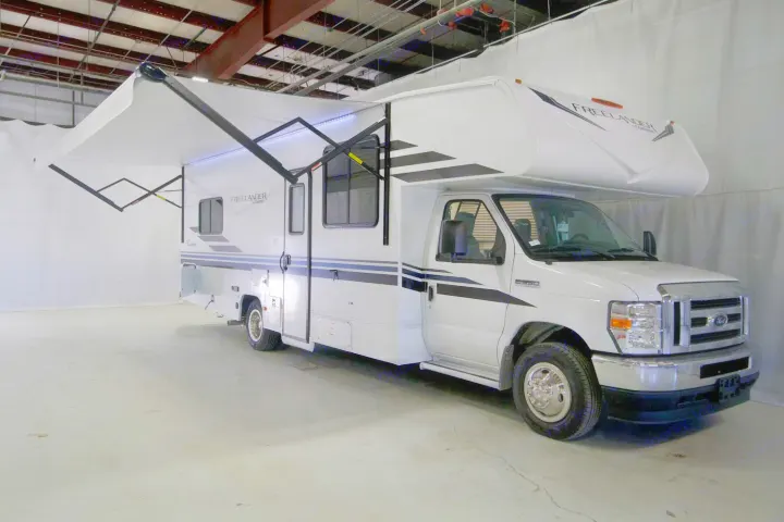 White RV rental motorhome featuring an extended awning with bright LED lights, parked indoors.. Freelander 27QB 2022