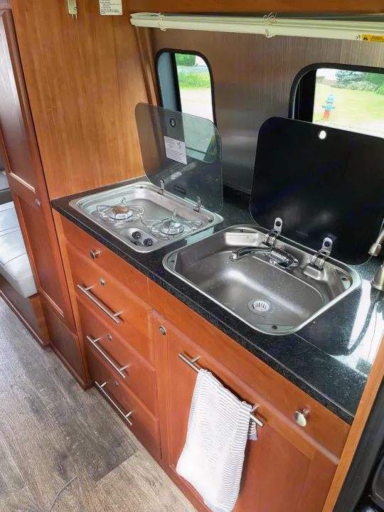 This RV rental features a compact kitchenette with a two-burner stove, sink, and ample wood cabinet storage for travel.. Roadtrek Roadtrek Class B 2015
