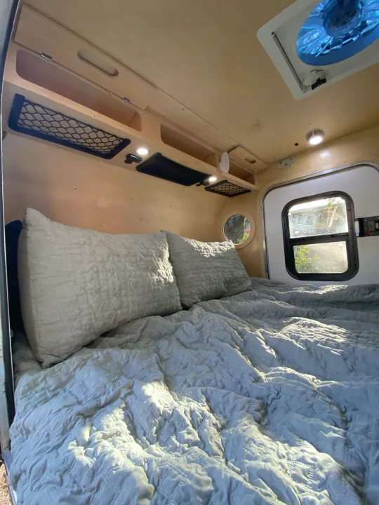 Cozy interior of an RV rental showing a comfortable bed, wooden walls, and natural light from a window.. Teardrops Northwest Trek 2022