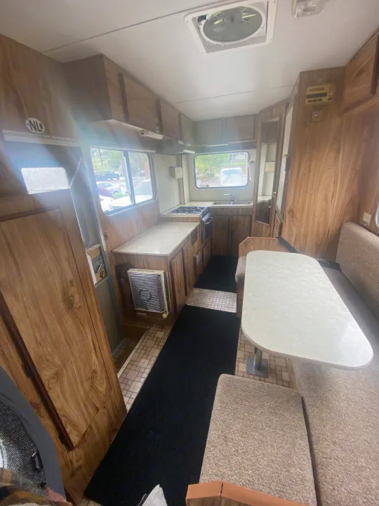 Spacious RV rental interior featuring a cozy dinette, functional kitchen, and warm wood paneling throughout.. Vanguard Industries MV 1800 1981