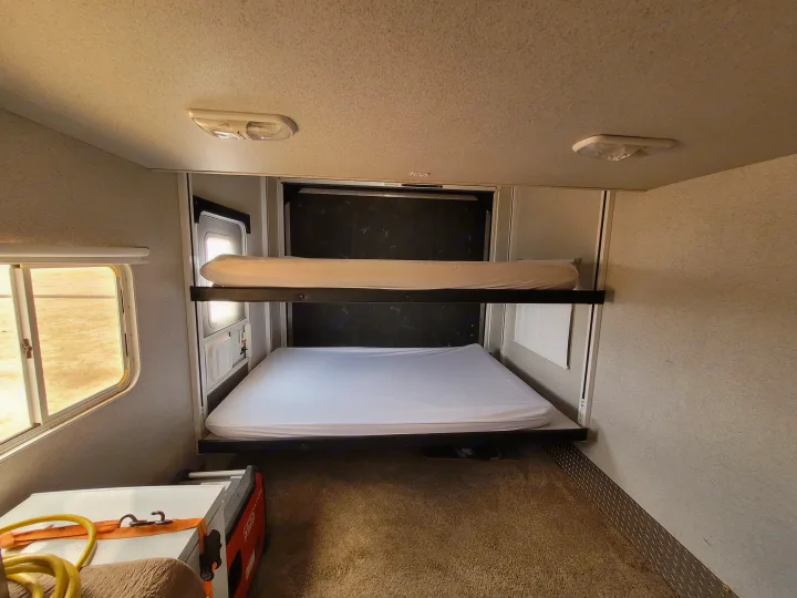 Interior of an RV rental: two stacked bunk beds with white mattresses, a window, and carpeted floor.. Heartland Cyclone 2009