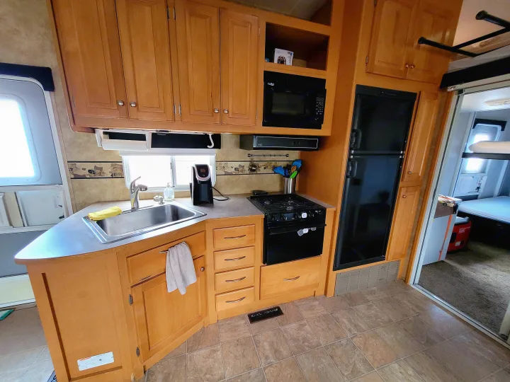 RV rental kitchen featuring wood cabinets, stainless steel sink, stove, microwave, and refrigerator.. Heartland Cyclone 2009