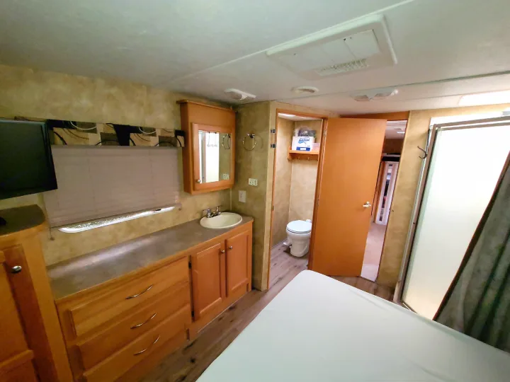 An RV rental featuring a bedroom with a vanity, sink, mirror, and an adjacent bathroom with a toilet and shower stall.. Heartland Cyclone 2009
