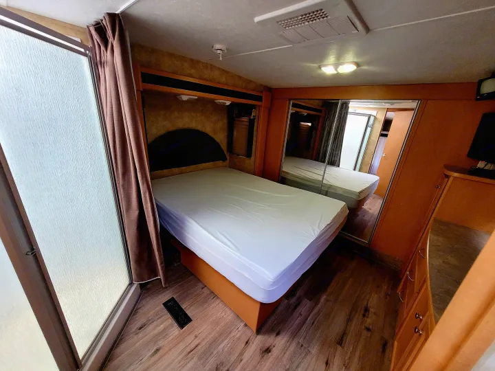 Interior of a clean RV rental bedroom, showing a comfortable bed, frosted glass shower, and mirrored closet doors.. Heartland Cyclone 2009
