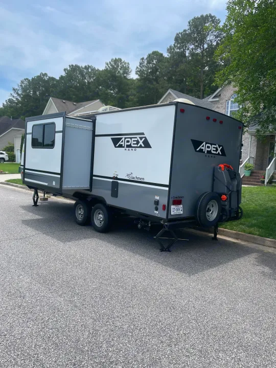 An Apex Nano travel trailer, a spacious RV rental option, is parked on a residential street with its slide-out extended.. Coachmen Apex Nano 2021