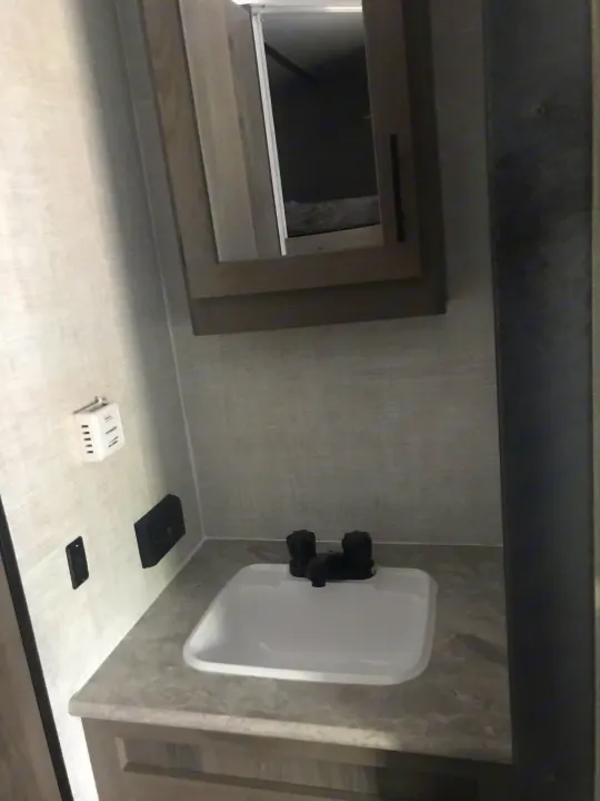 Compact RV rental bathroom featuring a sink, black faucet, and mirrored cabinet above, ideal for travel.. 1NL1G2725N6008015 ENLIGHTEN 2022