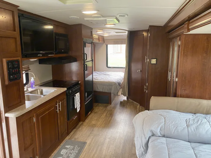 RV rental interior: kitchen (sink, stove, microwave), bedroom (bed), and living area (couch). Ample cabinets, wood-look floor.. Forest River 23DS 2018