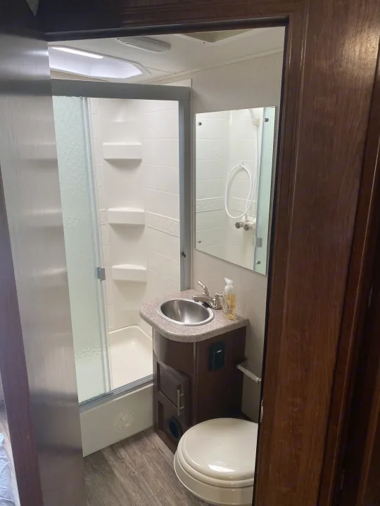 An RV rental bathroom showing a compact layout with standing shower, sink vanity, and toilet.. Forest River 23DS 2018