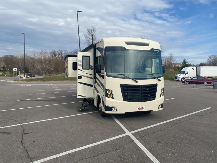 An RV rental, a cream-colored Forest River FR3 motorhome, is parked in a large asphalt lot with its side door open.. Forest River 23DS 2018