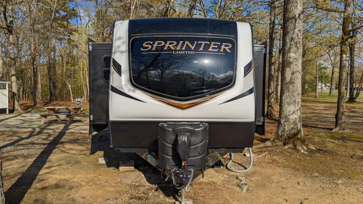 This Sprinter Limited RV, perfect for an RV rental, is parked amidst trees at a scenic campground.. Keystone RV Sprinter Limited 2021