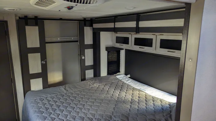 Spacious RV rental bedroom featuring a bed, overhead storage, and a barn-style closet door.. Keystone RV Sprinter Limited 2021
