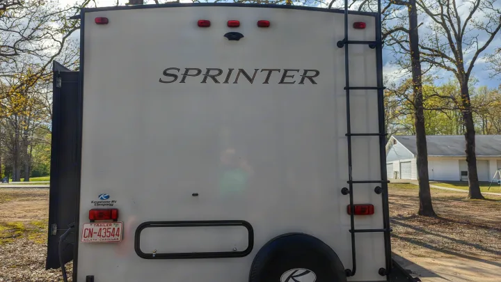 Rear of a Sprinter RV, featuring a ladder & spare tire, parked outdoors. Book this RV rental for your next adventure.. Keystone RV Sprinter Limited 2021