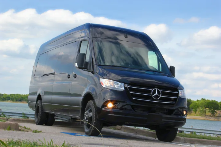 Black Mercedes-Benz Sprinter van, perfect for RV rental adventures, parked by a lake. Headlights on.. Mercedez Benz Sprinter 2020