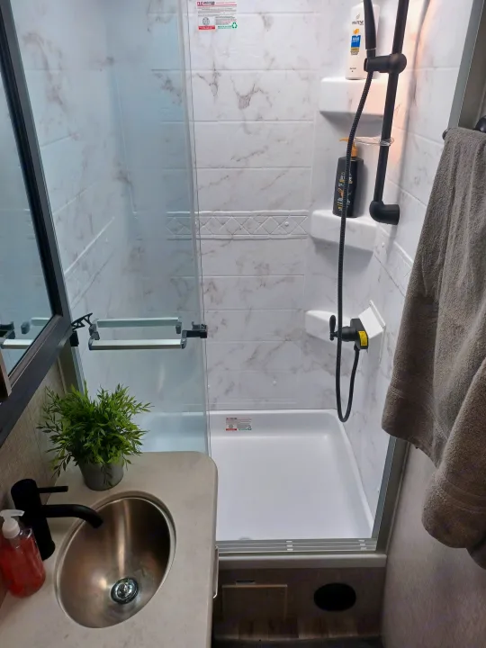 Modern RV rental bathroom featuring a marble-look shower with black fixtures and a compact sink vanity.. ENTEGRA VISION A27 2022