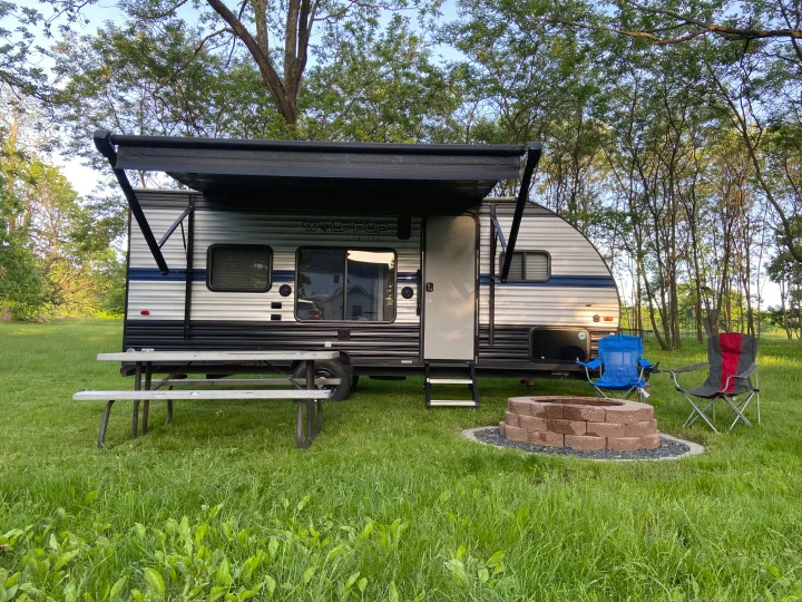 Setup for your next adventure: an RV rental with awning, picnic table, and fire pit in a grassy camp.. Forest River Cherokee Wolf Pup 2019