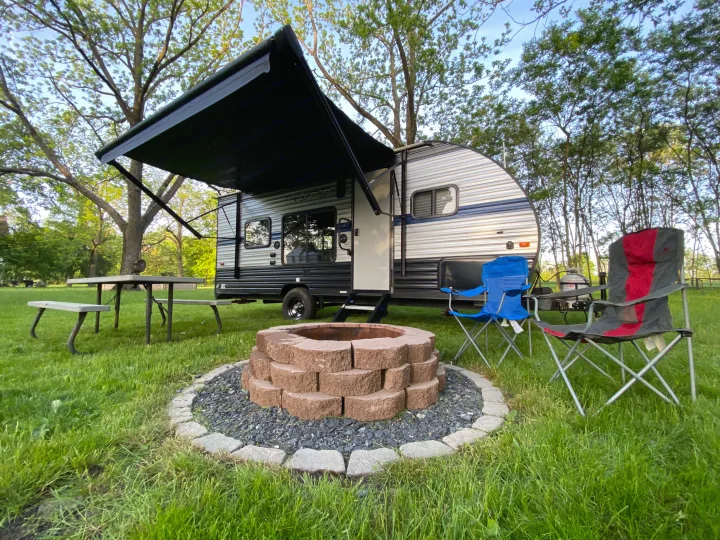 An RV rental set up at a scenic campsite with a fire pit, picnic table, and chairs, ready for outdoor fun.. Forest River Cherokee Wolf Pup 2019
