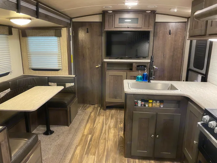 Cozy RV rental interior featuring a U-shaped dining booth, kitchen with sink & stove, and entertainment center.. Cruiser RV MPG Ultra Lite 2019