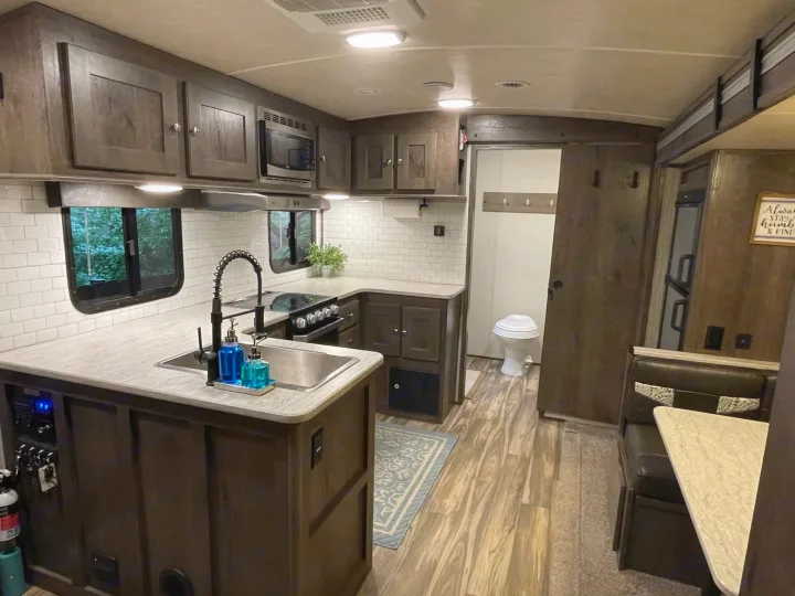 Modern RV rental interior showing a fully equipped kitchen with a sink, microwave, and adjacent dinette and bathroom.. Cruiser RV MPG Ultra Lite 2019