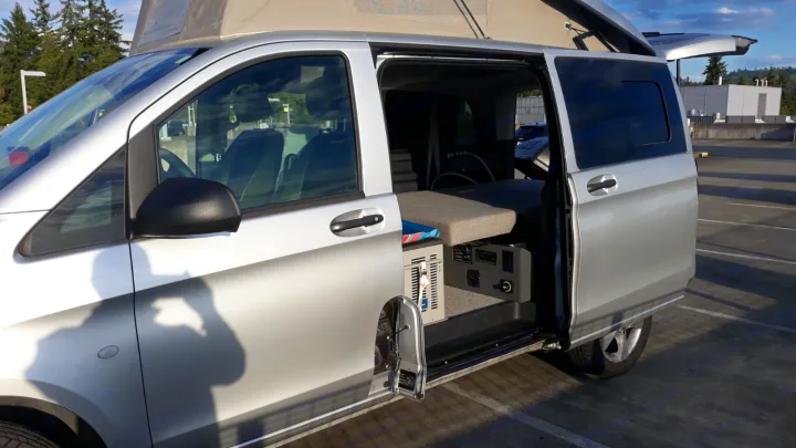 Silver camper van with pop-top roof and open side door revealing its compact interior setup, great for an RV rental.. Mercedes Metris 2016