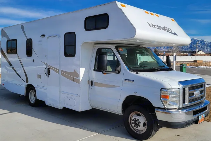 Bright white Majestic Class C RV rental, built on a Ford E-350 chassis, parked outdoors with a mountain backdrop.. THOR MAJESTIC 23a 2018
