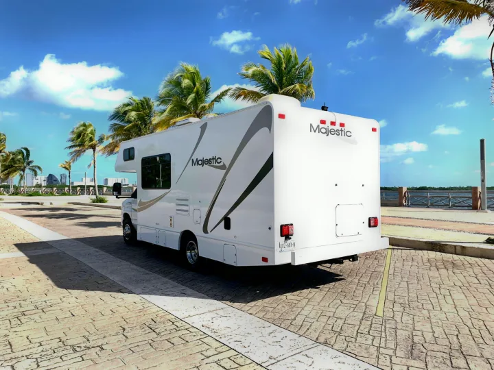 A white Majestic rv rental parked by palm trees & water under a bright blue sky. Perfect for a sunny coastal road trip.. THOR MAJESTIC 23a 2018