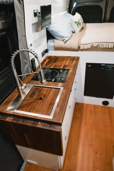 Discover this stylish rv rental! Features a modern kitchen with wood counters, sink, and induction cooktop, plus a cozy bed and fridge.. Other Other 2021