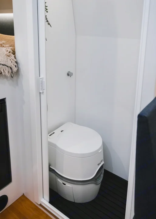 Compact RV rental bathroom featuring a white portable toilet, wall-mounted faucet, and dark, ribbed floor.. Other Other 2021