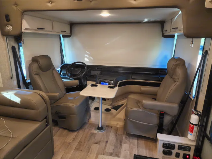 This RV rental's inviting cockpit showcases comfortable captain's chairs, a steering wheel, dashboard, and a central table.. Jayco Alante 2022