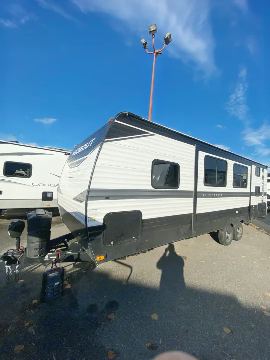 A large white and black Keystone Hideout travel trailer, ideal for rv rental, parked outdoors on a bright, sunny day.. Keystone RV Hideout 2022