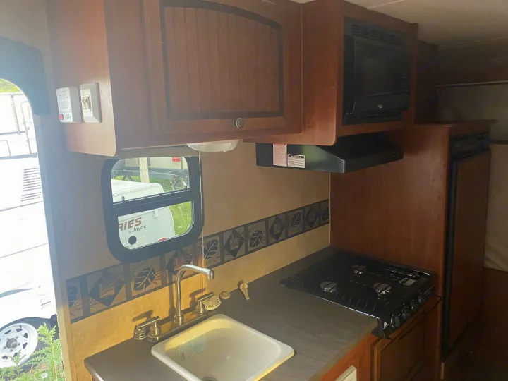 RV rental interior: A compact kitchen with microwave, gas stove, sink, and wood cabinetry, ready for your road trip.. Jayco Jay Feather Ultra Lite 2012