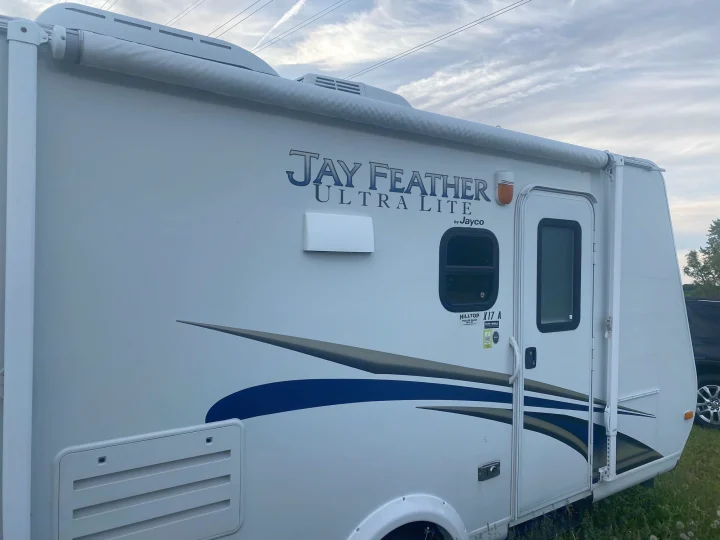 White Jay Feather Ultra Lite travel trailer, a perfect RV rental. Its side shows an awning, door, and windows.. Jayco Jay Feather Ultra Lite 2012