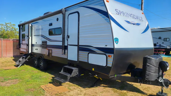 Bright Springdale travel trailer, perfect as an RV rental, parked on grass. Steps and a 'HELLO' mat welcome guests.. Keystone Springdale 2022
