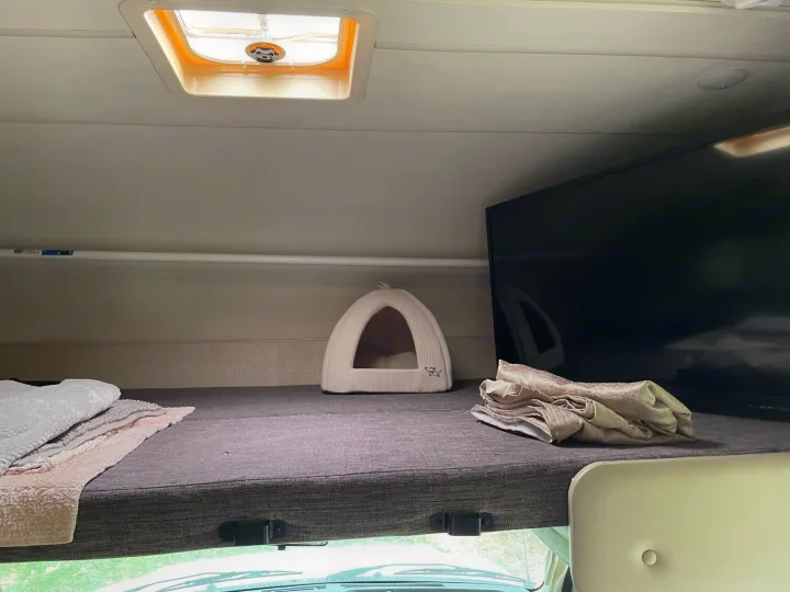 Cozy rv rental overhead bunk: pet bed, folded blankets, and mounted TV. Ready for comfortable travel adventures.. Thor Four Winds 2018