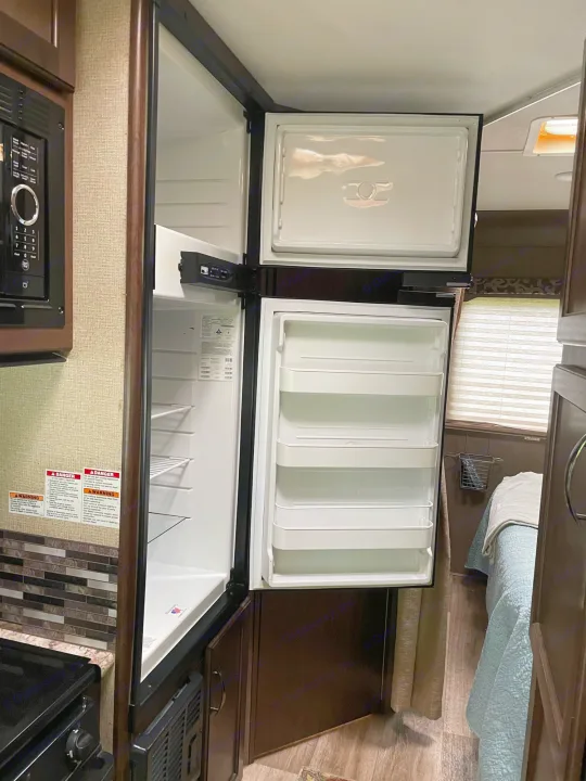 Inside an RV rental: kitchen area with open refrigerator, microwave, and a cozy bedroom section visible beyond.. Thor Four Winds 2018