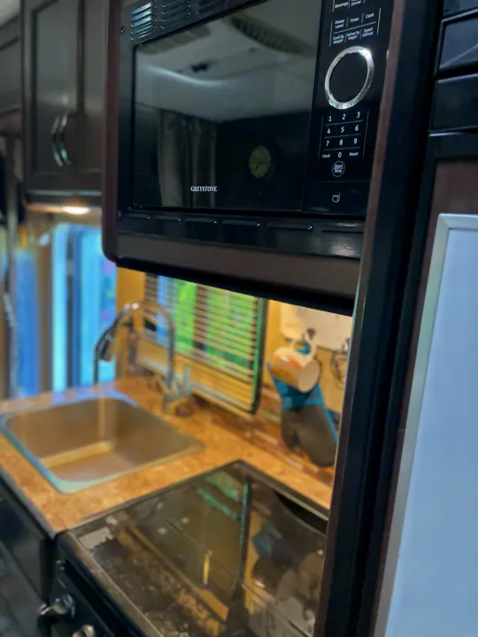A compact RV rental kitchen area features a Greystone microwave above a sink and stovetop.. Thor Four Winds 2018