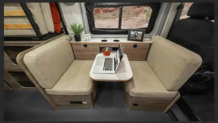 RV rental interior: cozy dinette with laptop on table, cushioned seating, and scenic window view. Ideal mobile workspace.. Winnebago pocket 2023